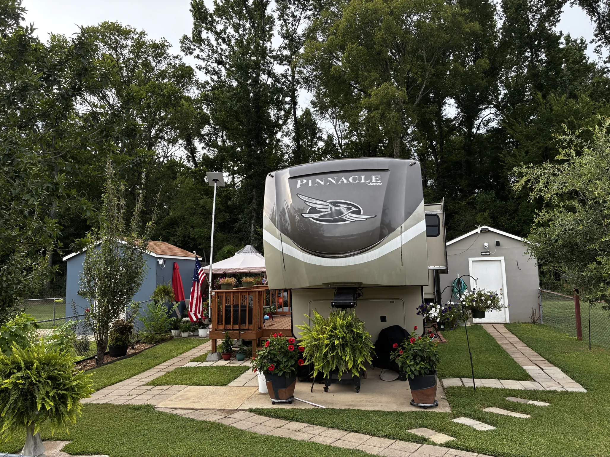 A fifth-wheel RV parked on a full-hookup site at Antique Capital RV Park with a wooden deck, potted flowers, and a paved walkway