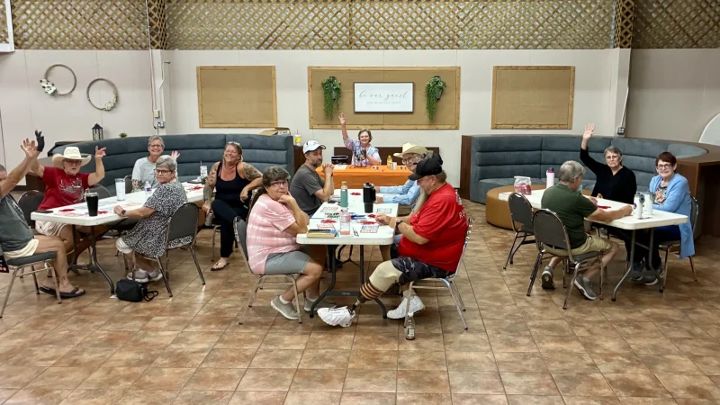 Park guests raising their hands during a bingo game at tables inside the Activity Center at Antique Capital RV Park