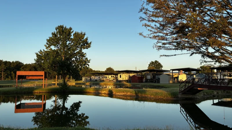 The private pond and footbridge at Antique Capital RV Park The private fishing pond and red footbridge at Antique Capital RV Park, with grassy lawns and covered RV sites in the evening light